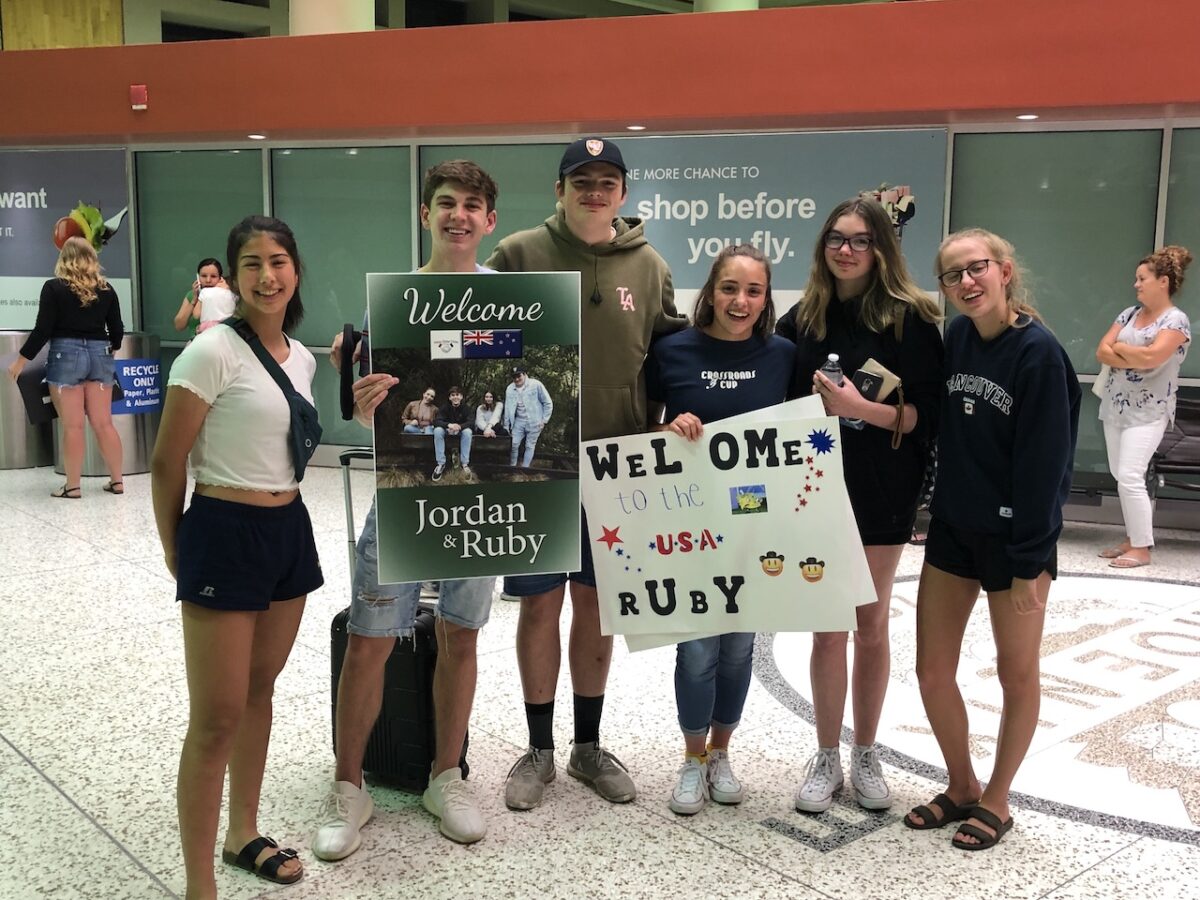 A group of high school ambassadors welcoming kids from another country at the airport with signs.