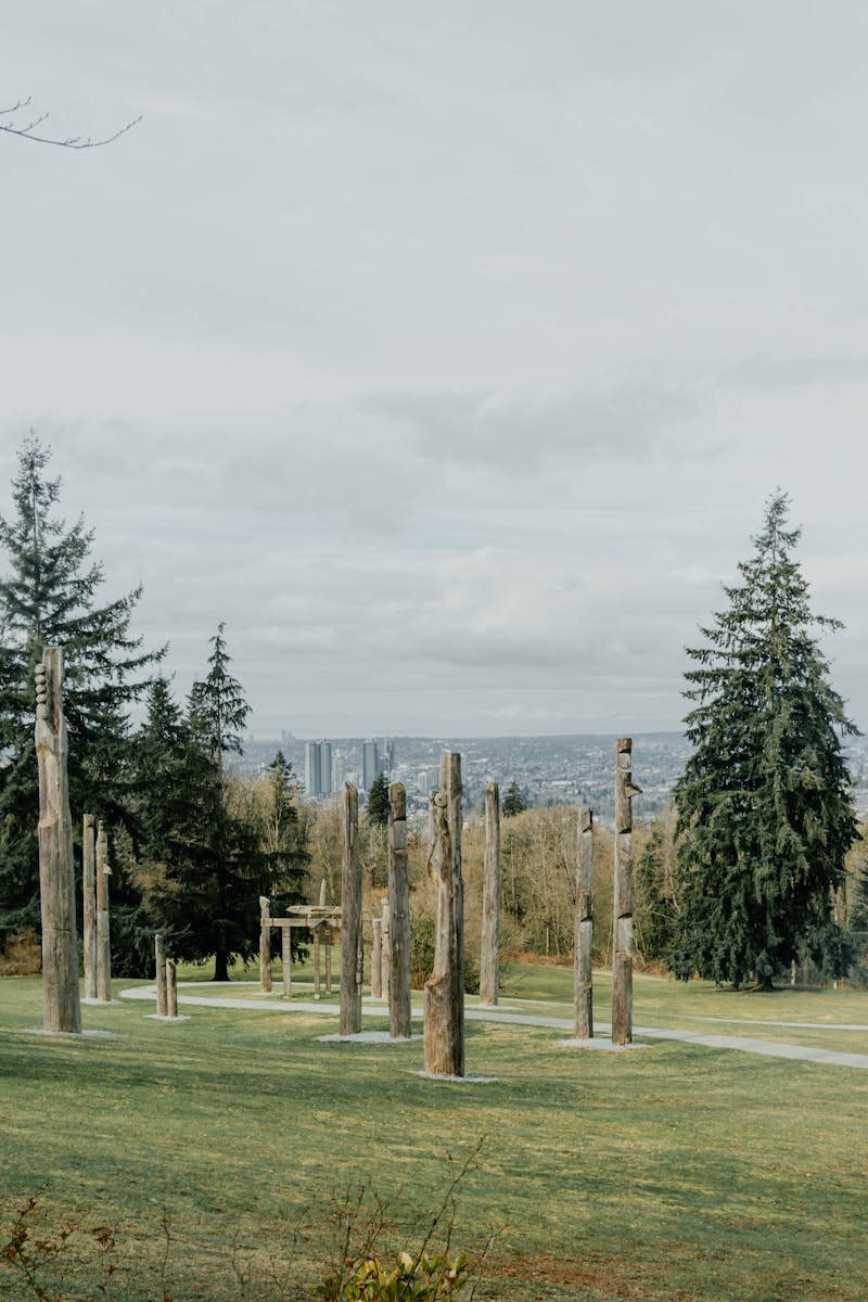 Totem pole installation at Burnaby Mountain Park, known as Kamui Mintara, overlooking the city skyline on a cloudy day.